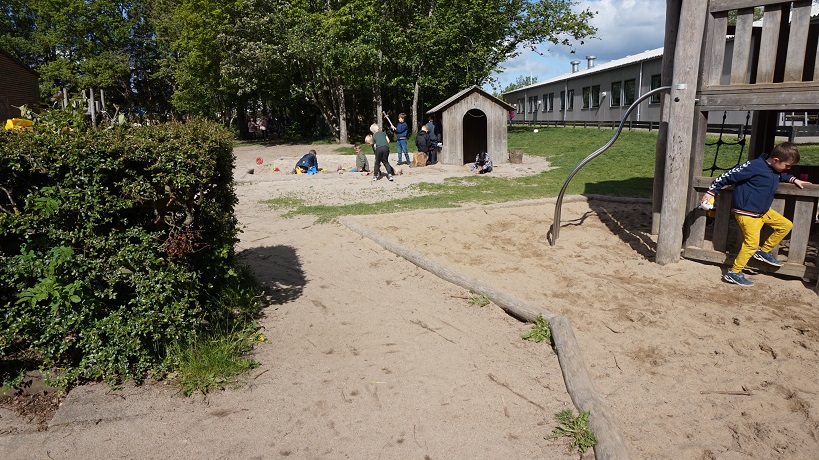Børn der leger i legehus og klatrestativ i en sandkasse.