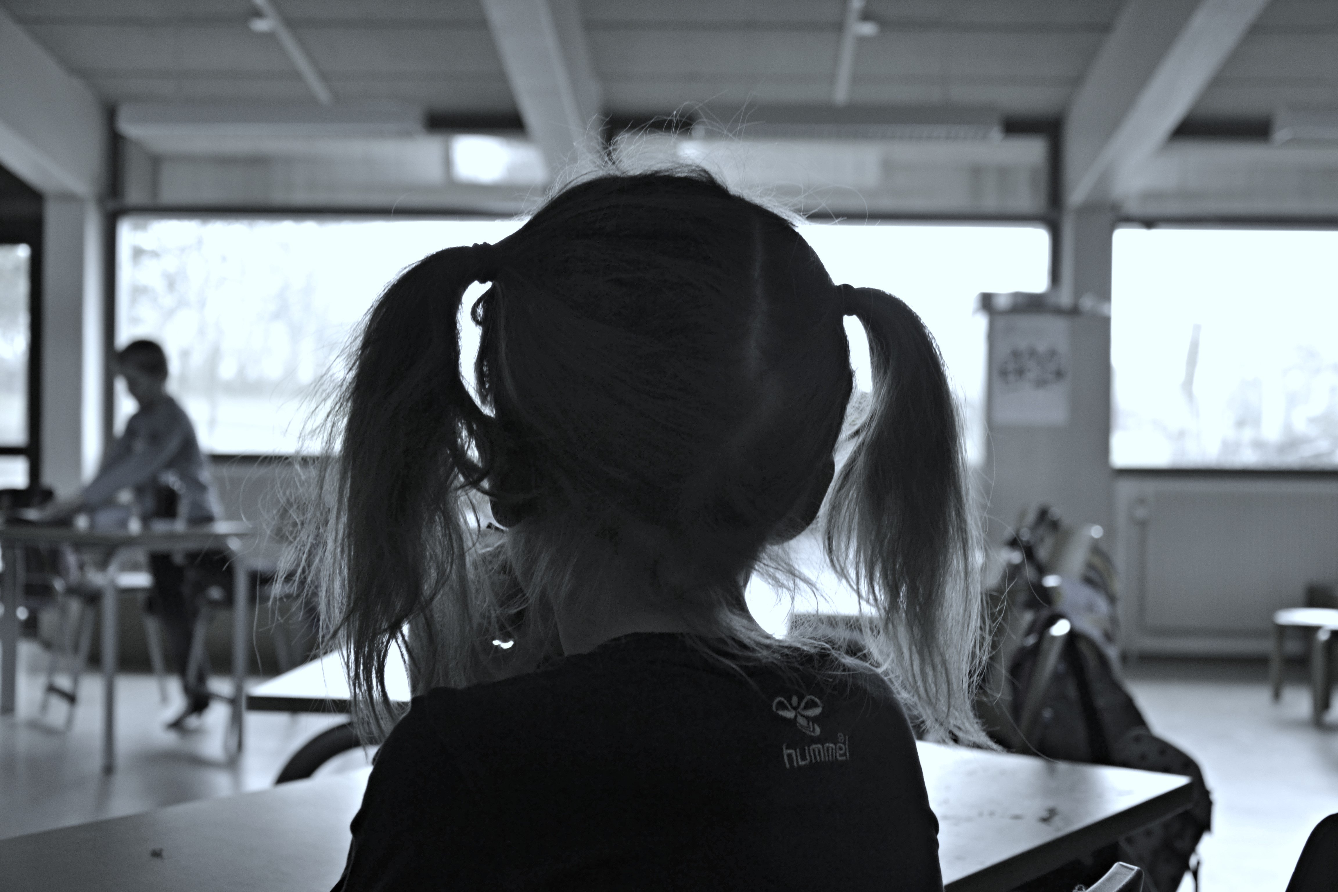 Sort hvid billede med et barn i en klasse der ser på de andre på afstand